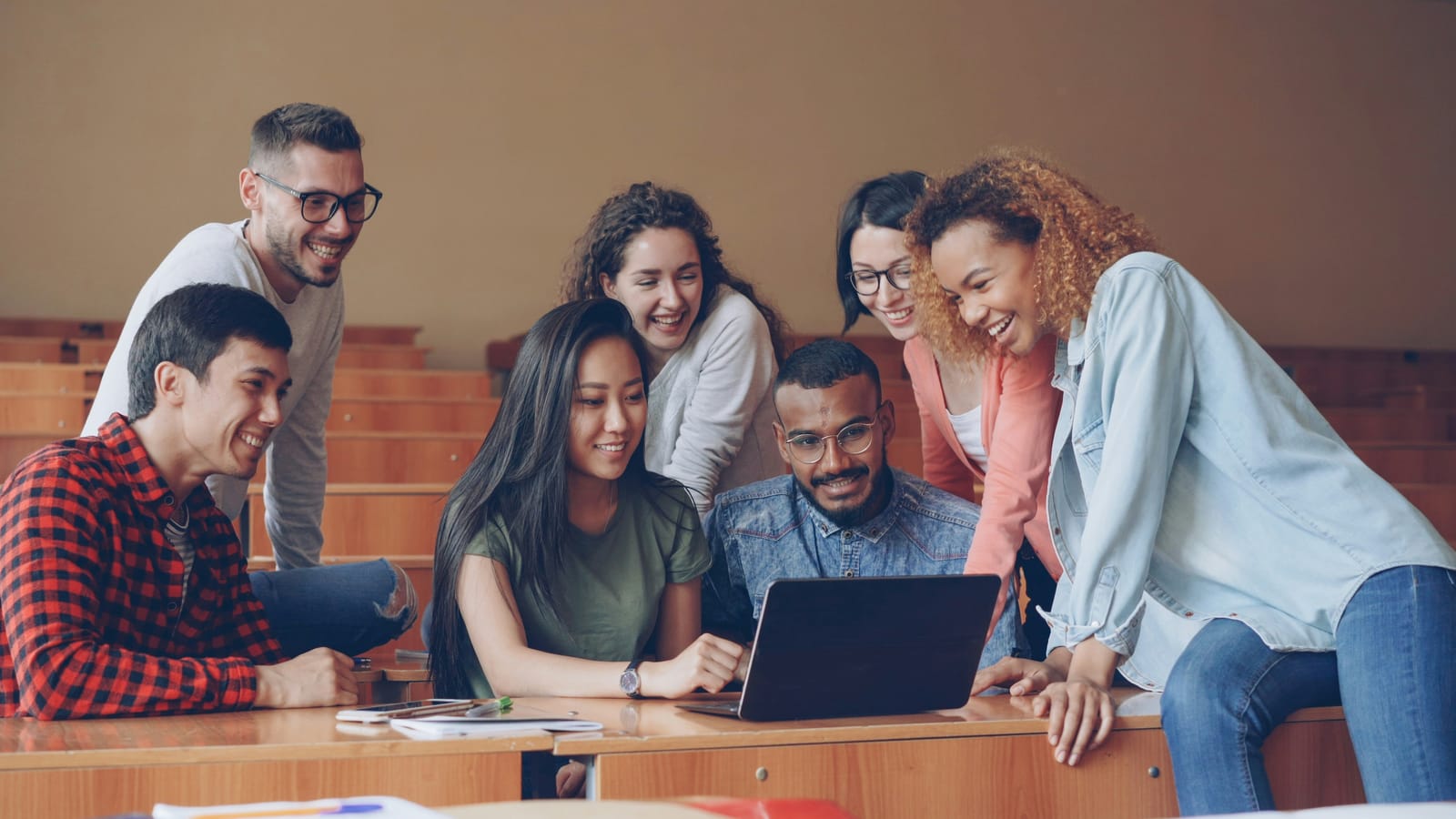 Grupo de jovens olha junto para a tela de um notebook em uma sala de estudos